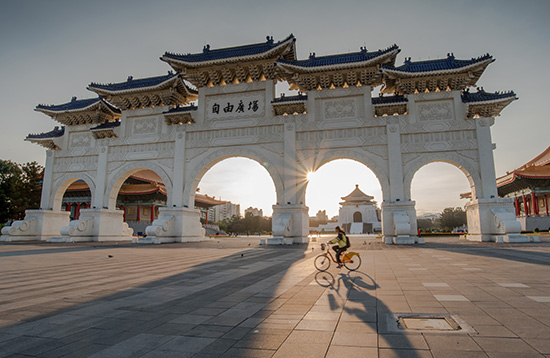 Cyclist rides past Liberty Square Arch in Taipei at sunset.